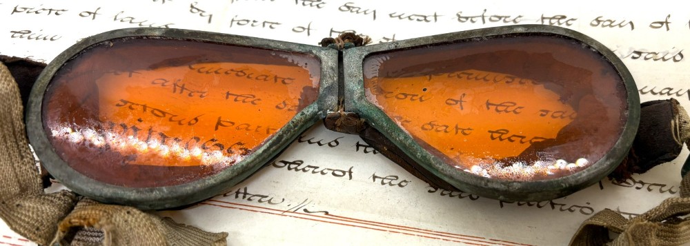 A pair of early 20th-century aviation goggles with amber glass lenses and a fabric strap resting alongside a brown storage case. View II