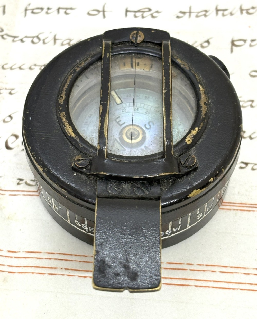 A circular black patinated brass military field compass featuring a central glass window, top sighting bar, and side directional markings.