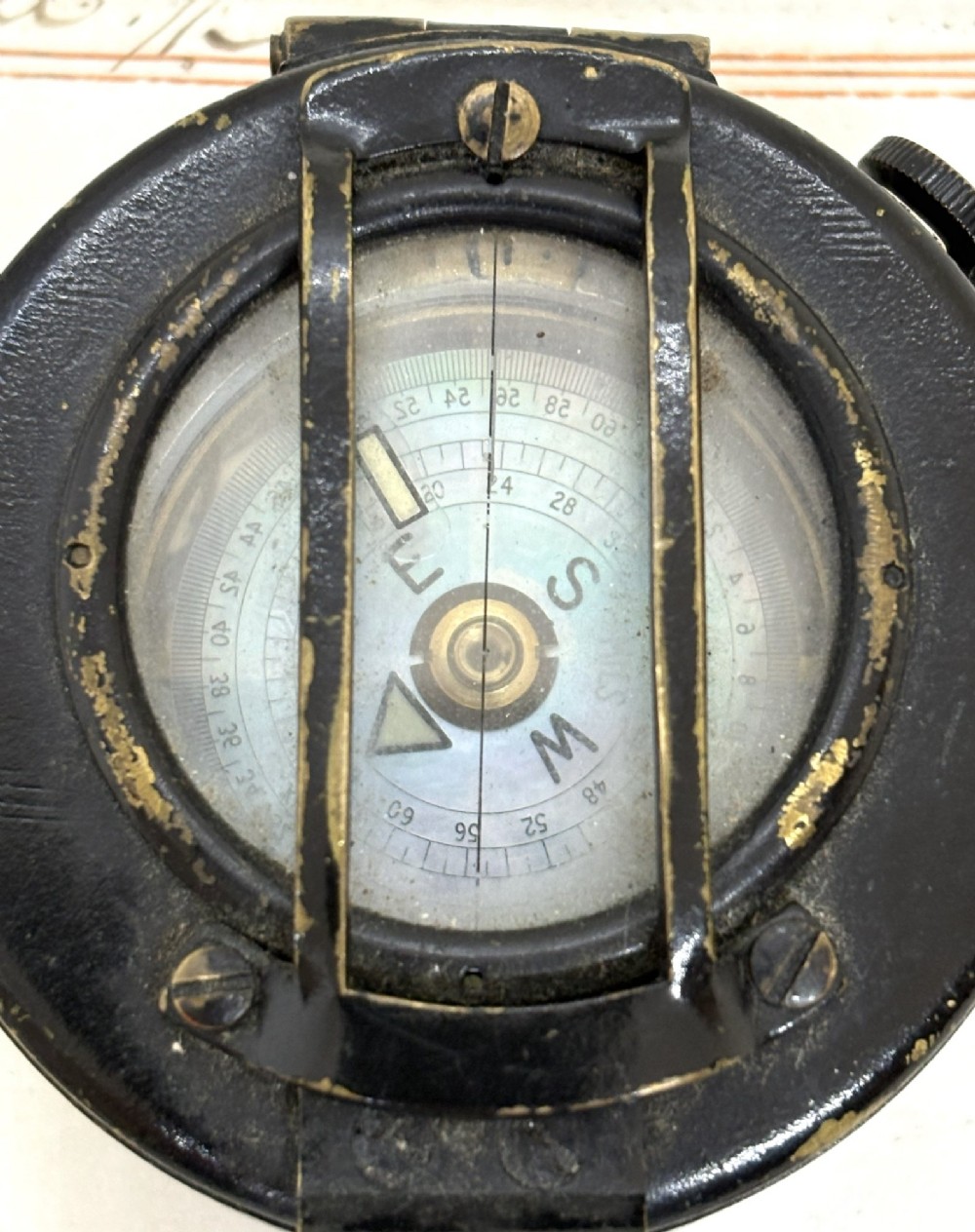 A circular black patinated brass military field compass featuring a central glass window, top sighting bar, and side directional markings. View V