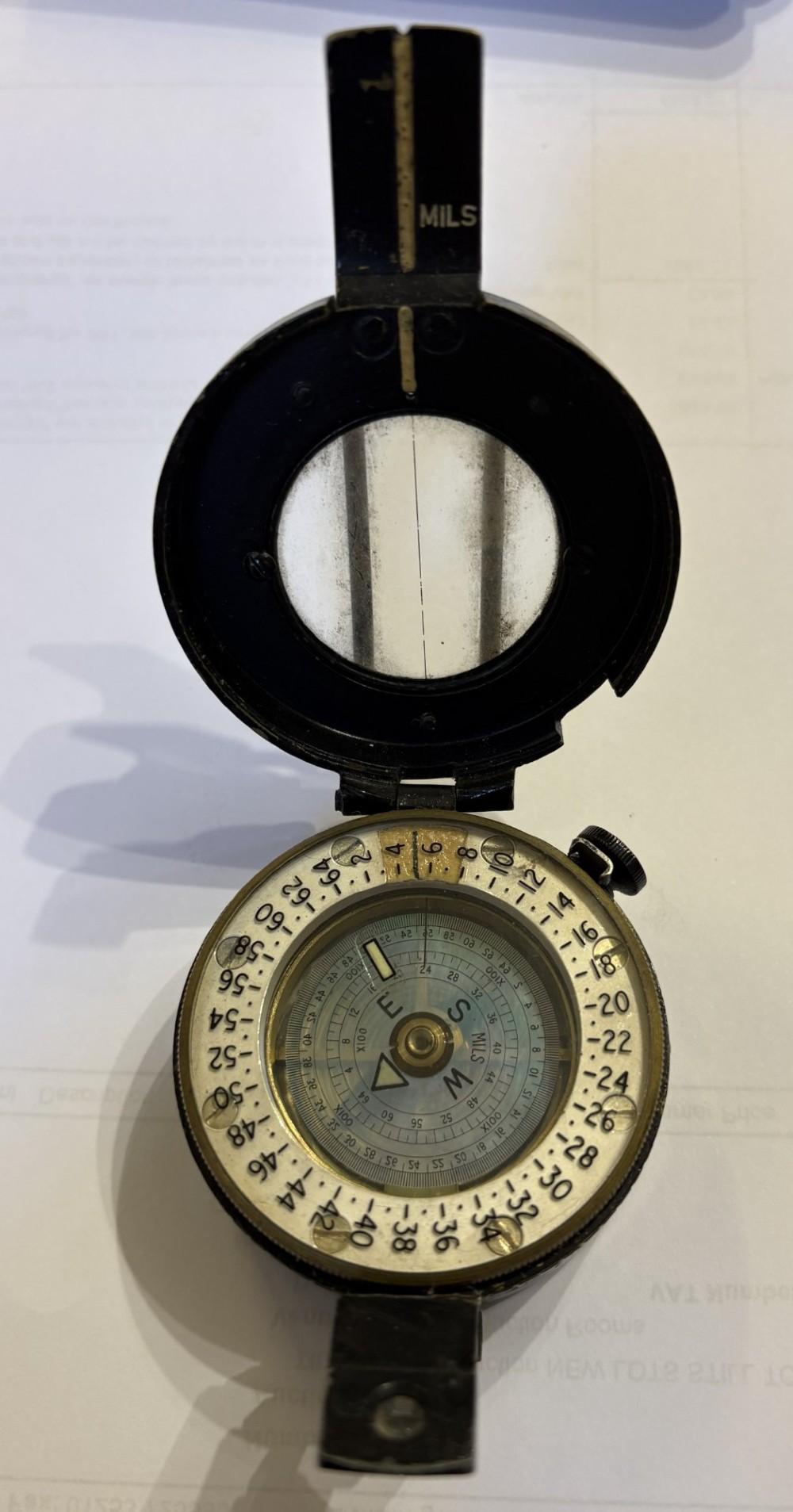 A circular black patinated brass military field compass featuring a central glass window, top sighting bar, and side directional markings. View VI