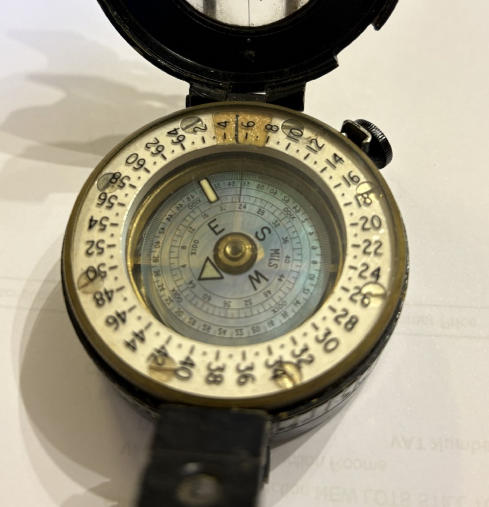 A circular black patinated brass military field compass featuring a central glass window, top sighting bar, and side directional markings. View VII