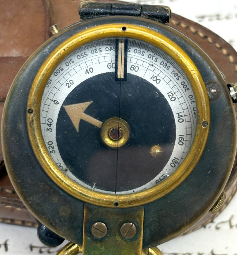 An antique brass pocket field compass resting on its original stitched brown leather protective case. View II