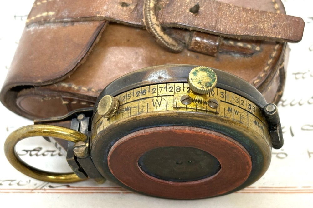 An antique brass pocket field compass resting on its original stitched brown leather protective case. View III