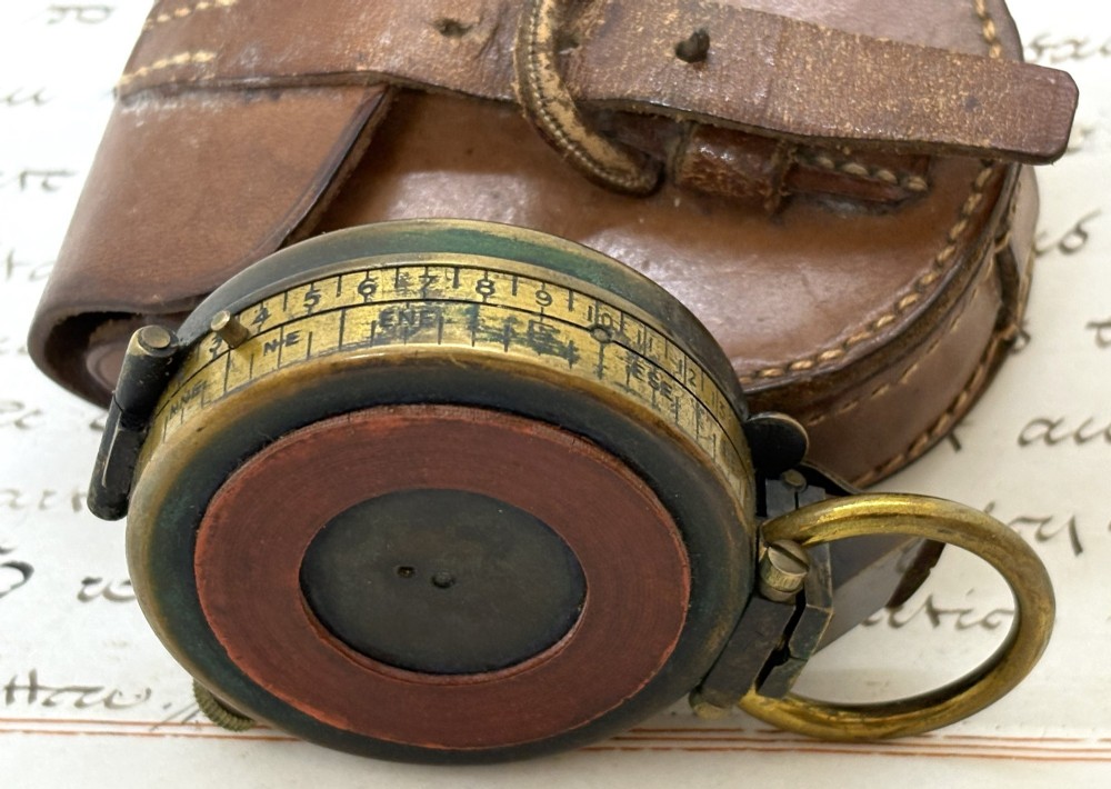 An antique brass pocket field compass resting on its original stitched brown leather protective case. View IV
