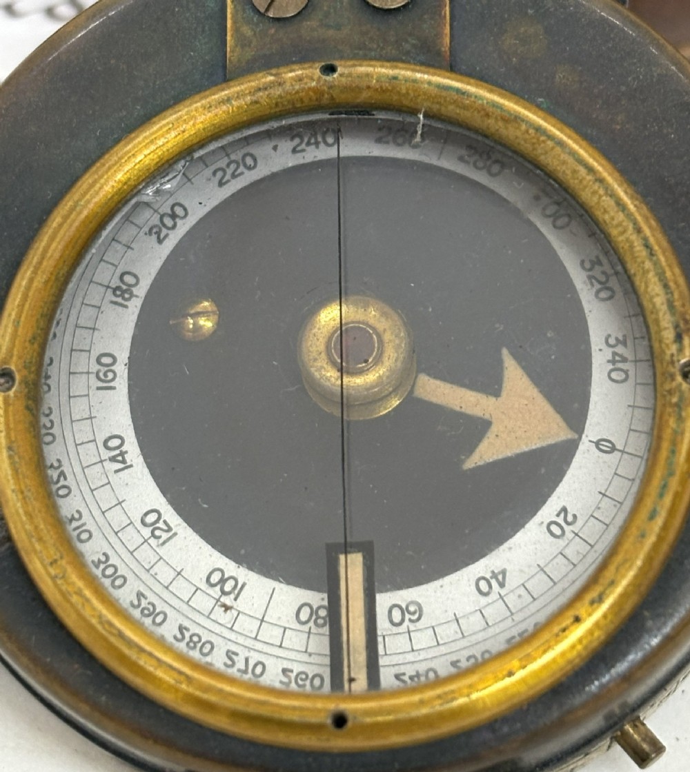 An antique brass pocket field compass resting on its original stitched brown leather protective case. View VI