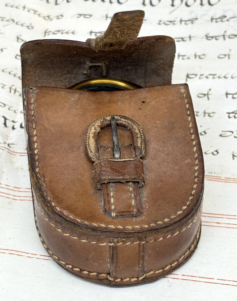 An antique brass pocket field compass resting on its original stitched brown leather protective case. View VII
