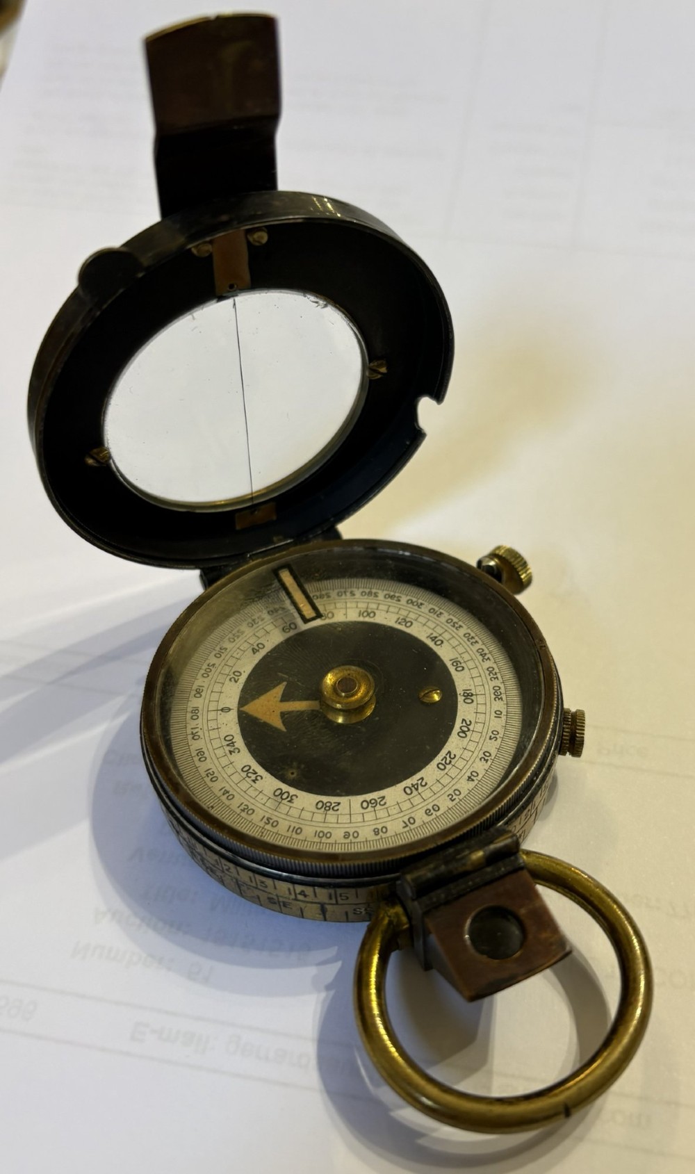 An antique brass pocket field compass resting on its original stitched brown leather protective case. View VIII