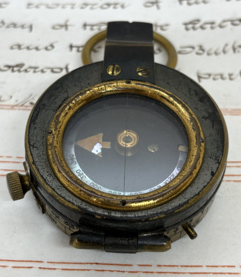 A First World War brass field compass with a patinated brass casing, glass crystal display, and fitted dark brown leather protective case. View II