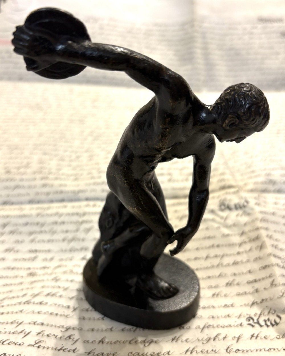 A dark patinated bronze figure depicting a male athlete in the classical Discobolus pose preparing to throw a discus.