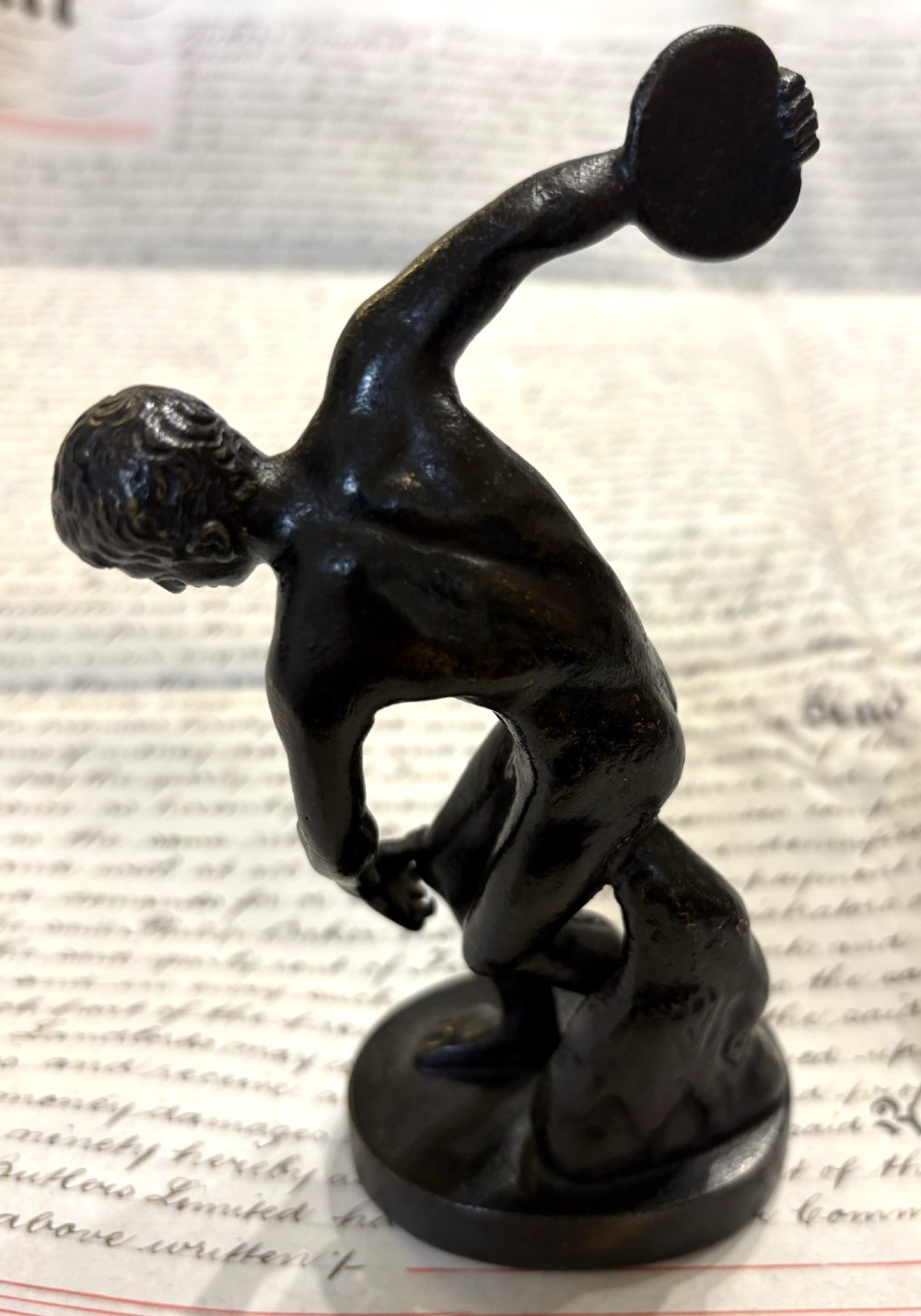 A dark patinated bronze figure depicting a male athlete in the classical Discobolus pose preparing to throw a discus. View II