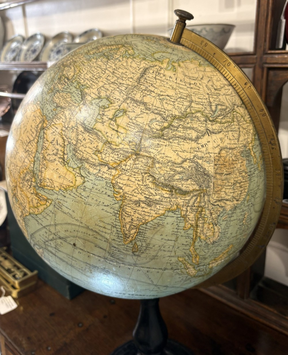 An antique French terrestrial globe featuring yellowed paper gores and pale blue oceans set within a brass meridian ring on an ebonised wooden base. View II
