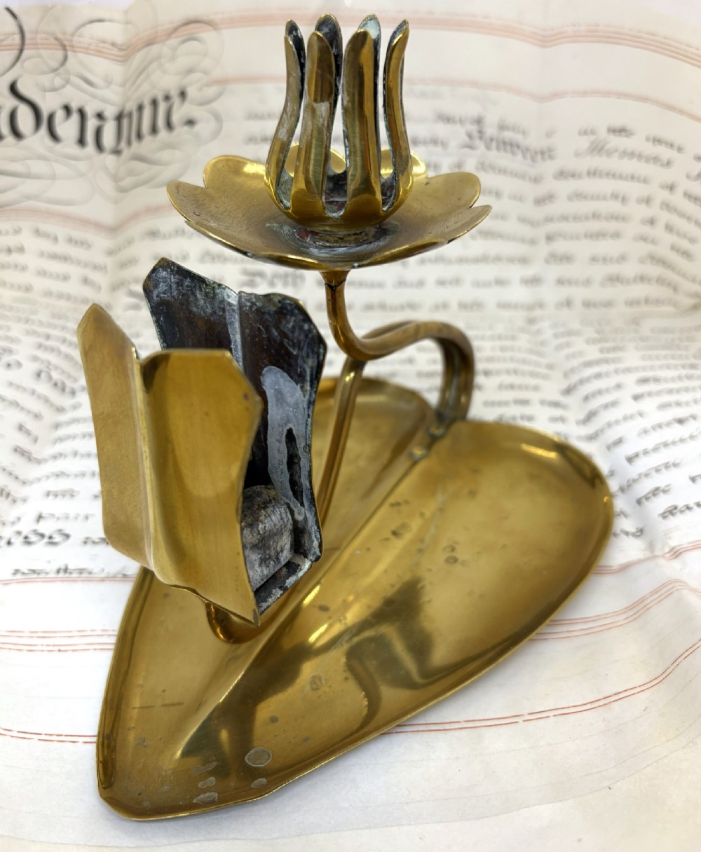 An Art Nouveau brass chamberstick featuring a leaf-shaped tray base, a curved stem supporting a tulip-form candle sconce, and an attached matchbox holder.