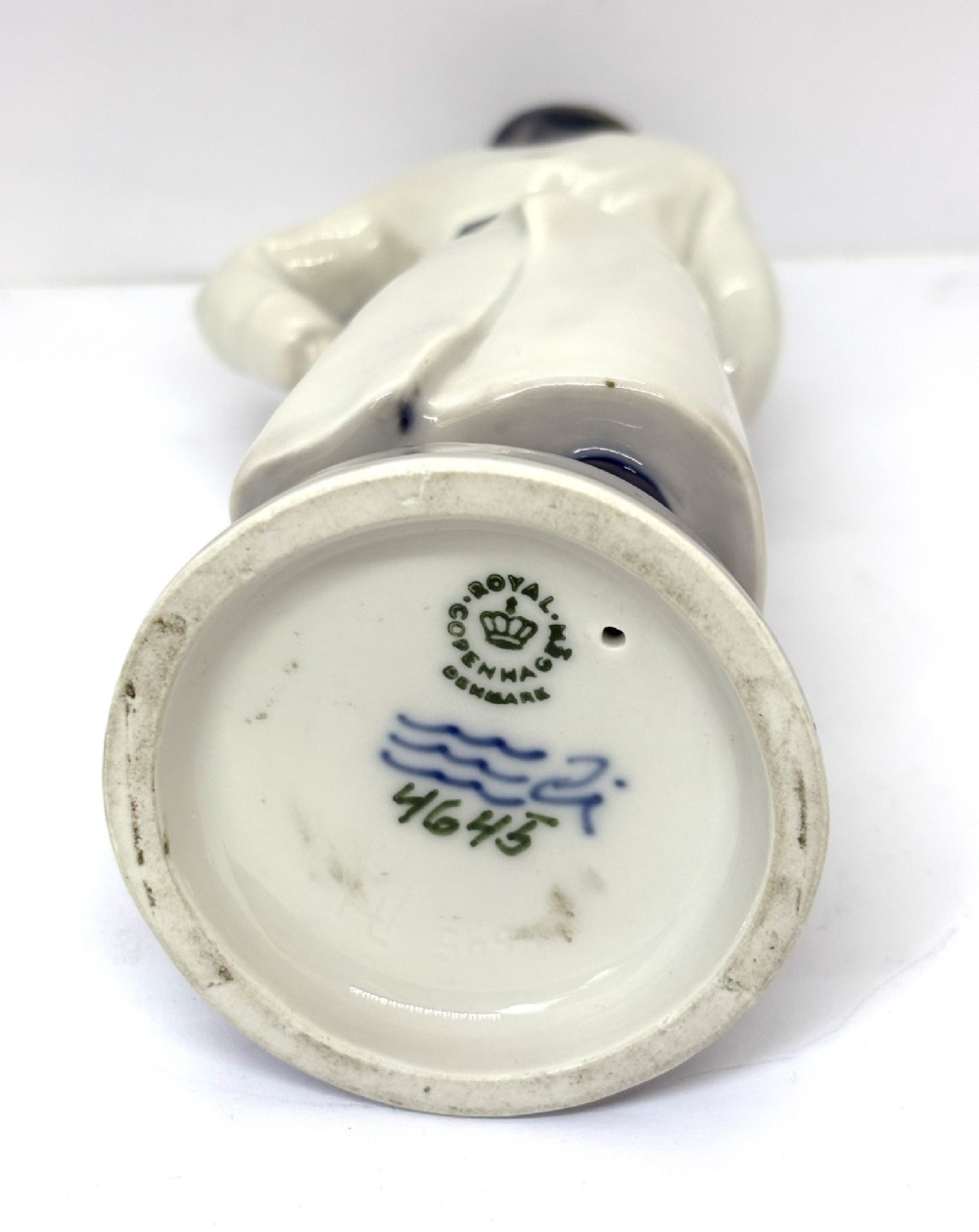 A glazed porcelain figurine depicting a butcher wearing a bowler hat, double-breasted coat, and apron standing beside a brown trough. View V