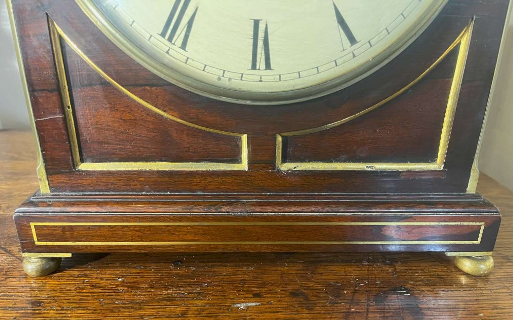 A Regency mahogany bracket clock featuring brass corner inlay, a top pineapple finial, brass ball feet, and a cream painted dial signed P. Ketterer Stamford Hill. View III