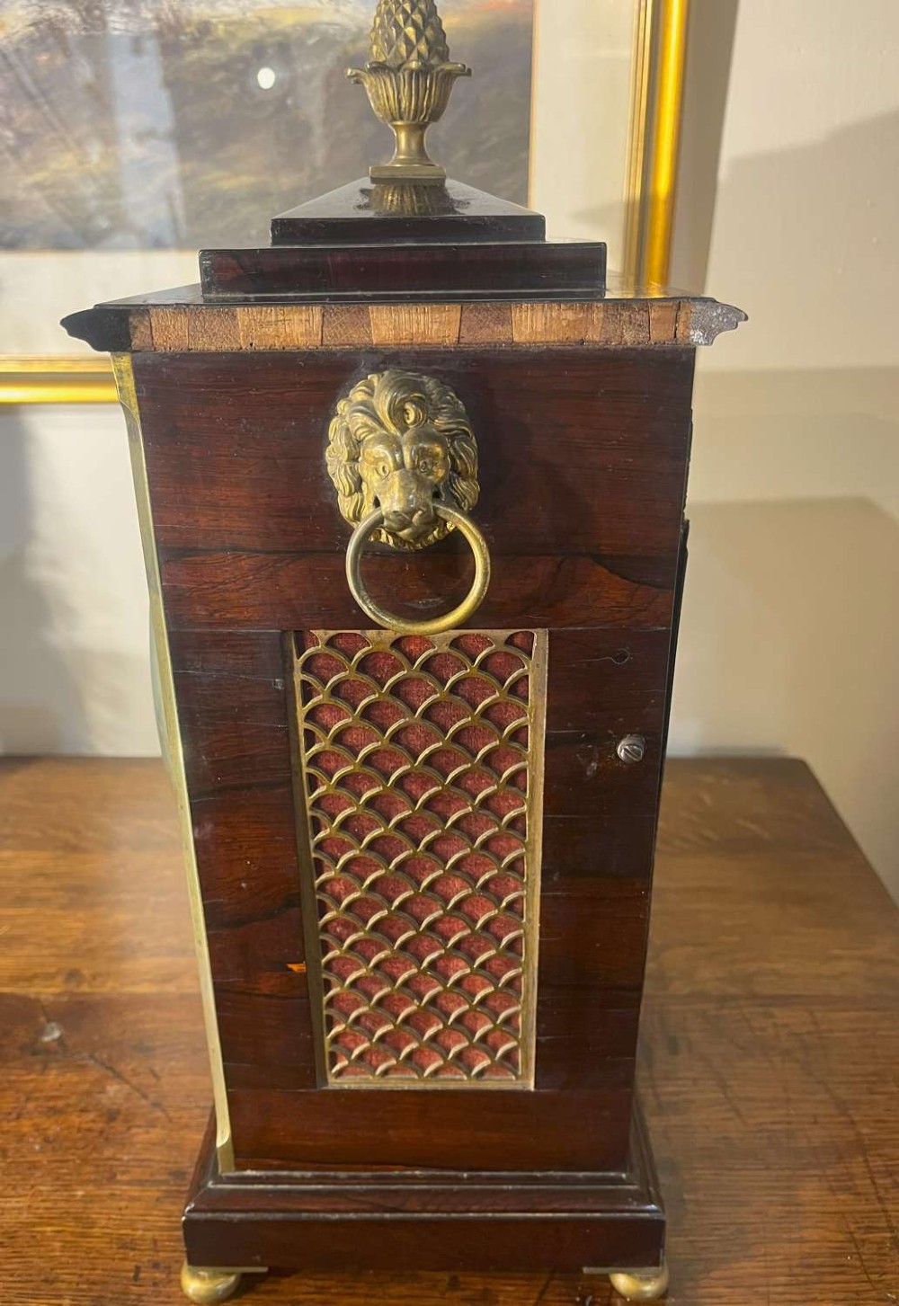 A Regency mahogany bracket clock featuring brass corner inlay, a top pineapple finial, brass ball feet, and a cream painted dial signed P. Ketterer Stamford Hill. View IV