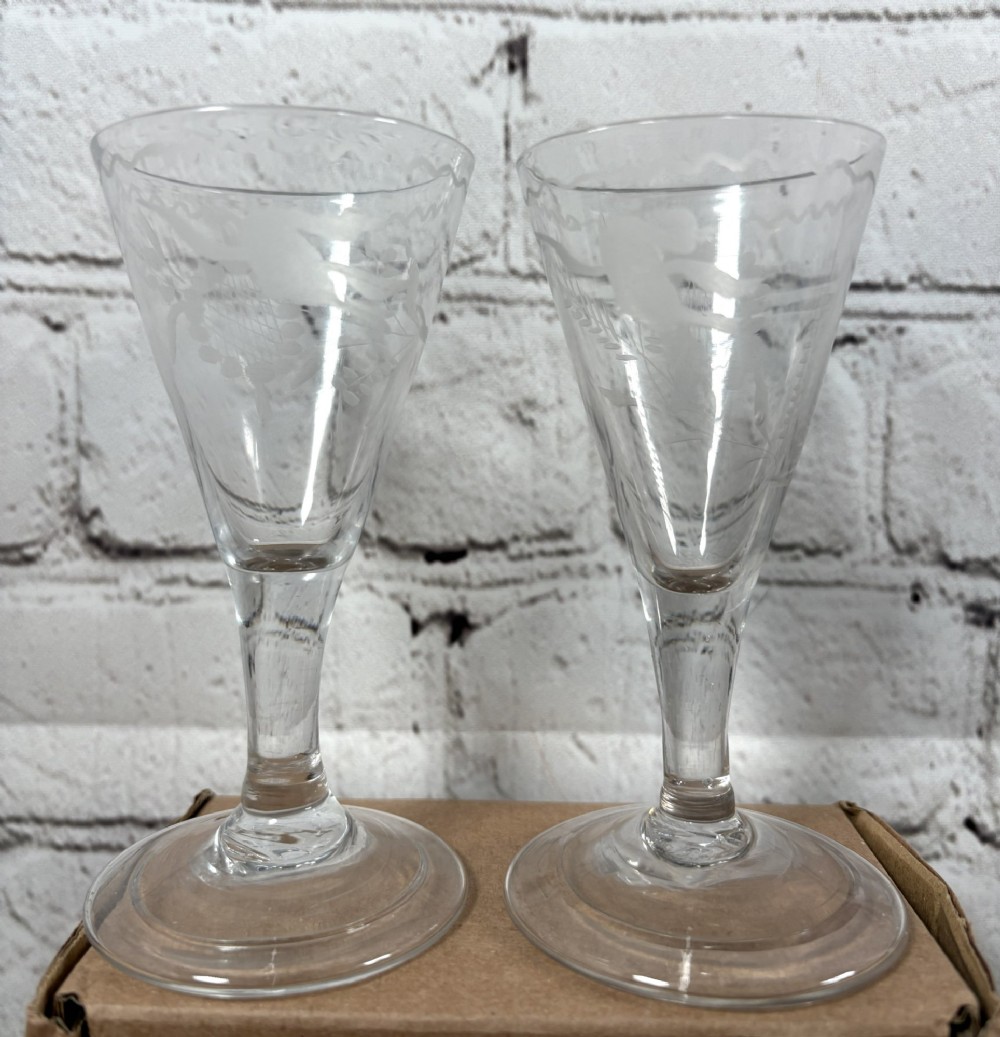 A pair of clear hand-blown Georgian glass drinking vessels featuring flared conical bowls with floral wheel engraving and circular bases.