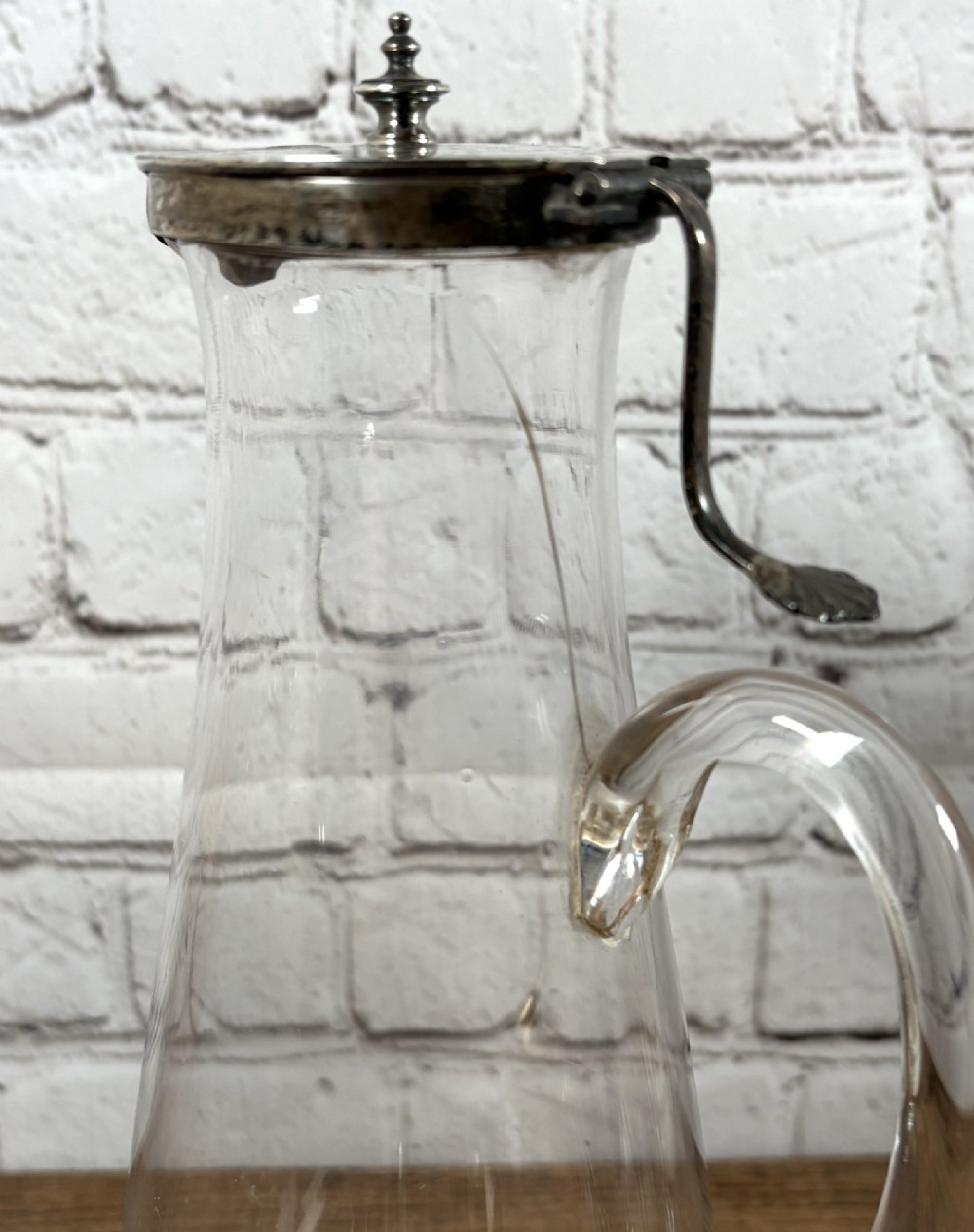 A clear glass claret jug featuring a starburst cut base, a loop glass handle, and an open hinged silver lid. View VII