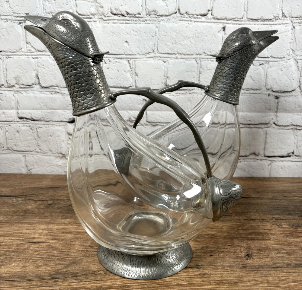A pair of clear glass claret jugs shaped like ducks with pewter heads, handles, tail caps, and circular bases. View II