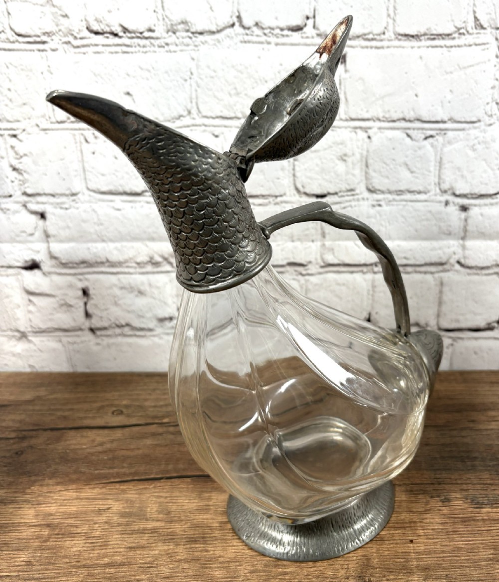 A pair of clear glass claret jugs shaped like ducks with pewter heads, handles, tail caps, and circular bases. View IV