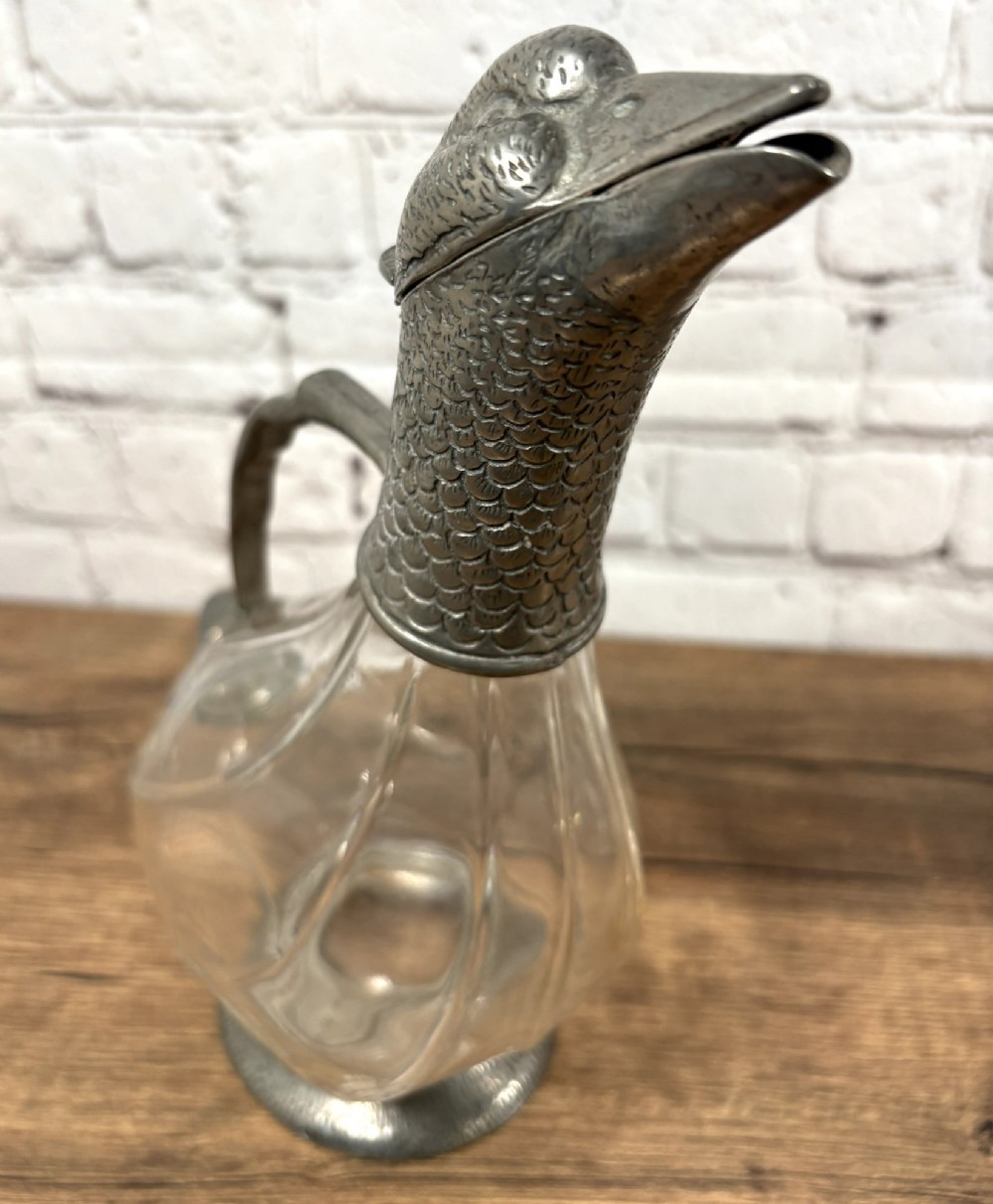 A pair of clear glass claret jugs shaped like ducks with pewter heads, handles, tail caps, and circular bases. View V