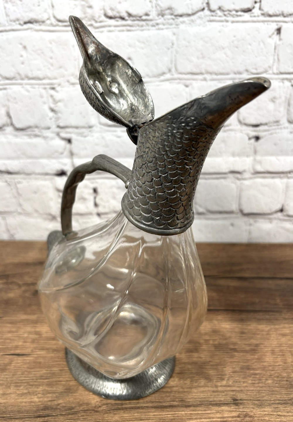 A pair of clear glass claret jugs shaped like ducks with pewter heads, handles, tail caps, and circular bases. View VI