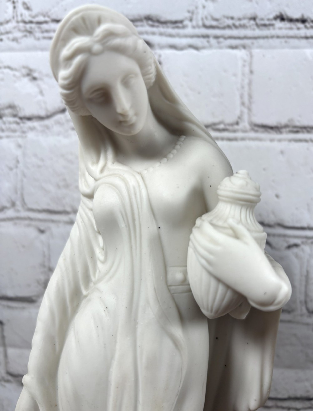 A pair of 19th-century unglazed white Parian ware porcelain figures depicting classical maidens in draped garments, standing on circular integrally moulded plinths. View V