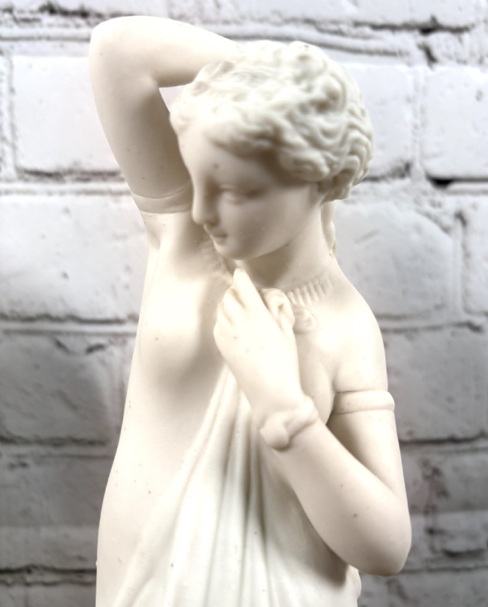 A pair of 19th-century unglazed white Parian ware porcelain figures depicting classical maidens in draped garments, standing on circular integrally moulded plinths. View VI