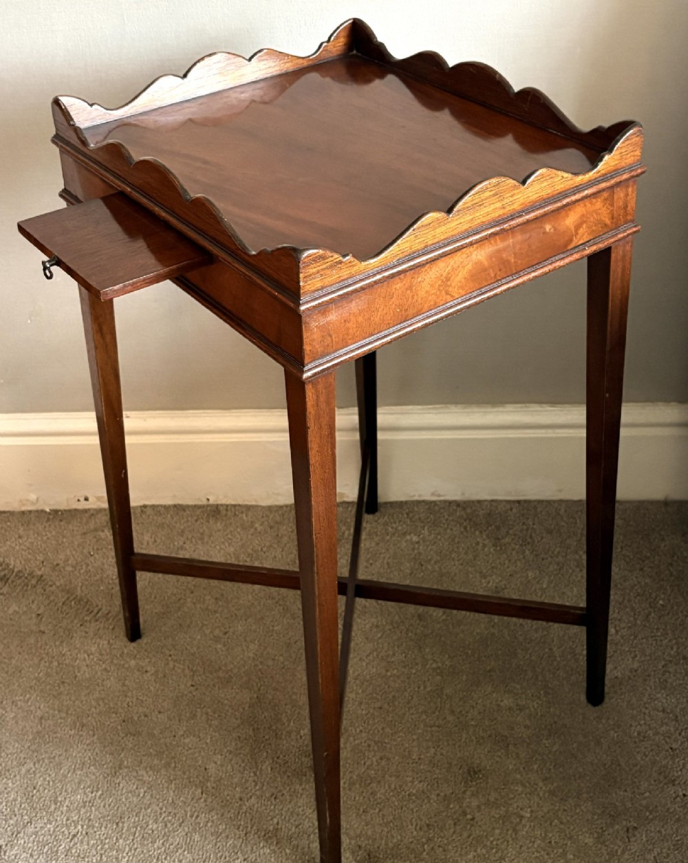 A mahogany kettle stand featuring a scalloped gallery top, a pull-out slide, slender square tapered legs, and an X-frame cross stretcher.