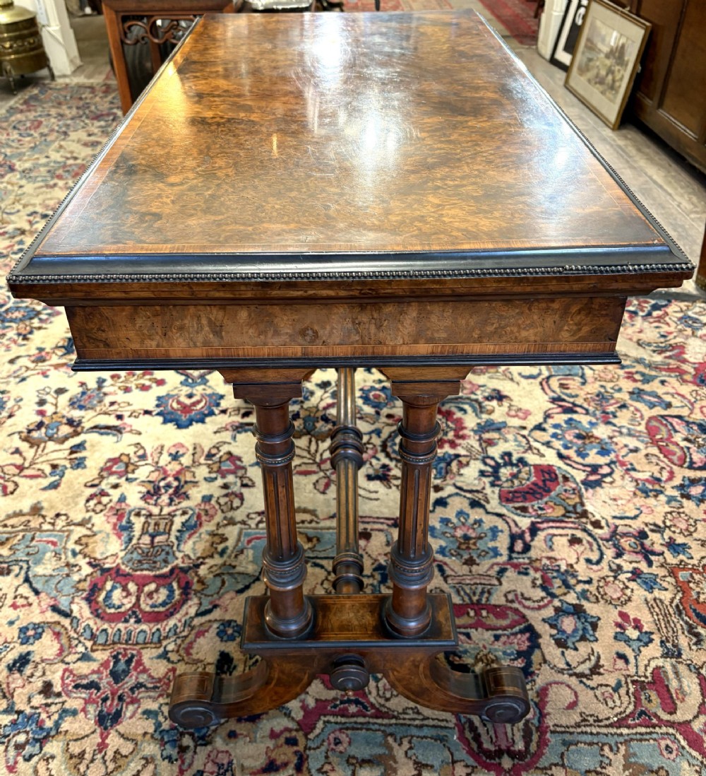 A Victorian burr walnut card table featuring ebonised bead moulding, crossbanded veneer top, twin turned pillar supports, and a turned stretcher base. View II