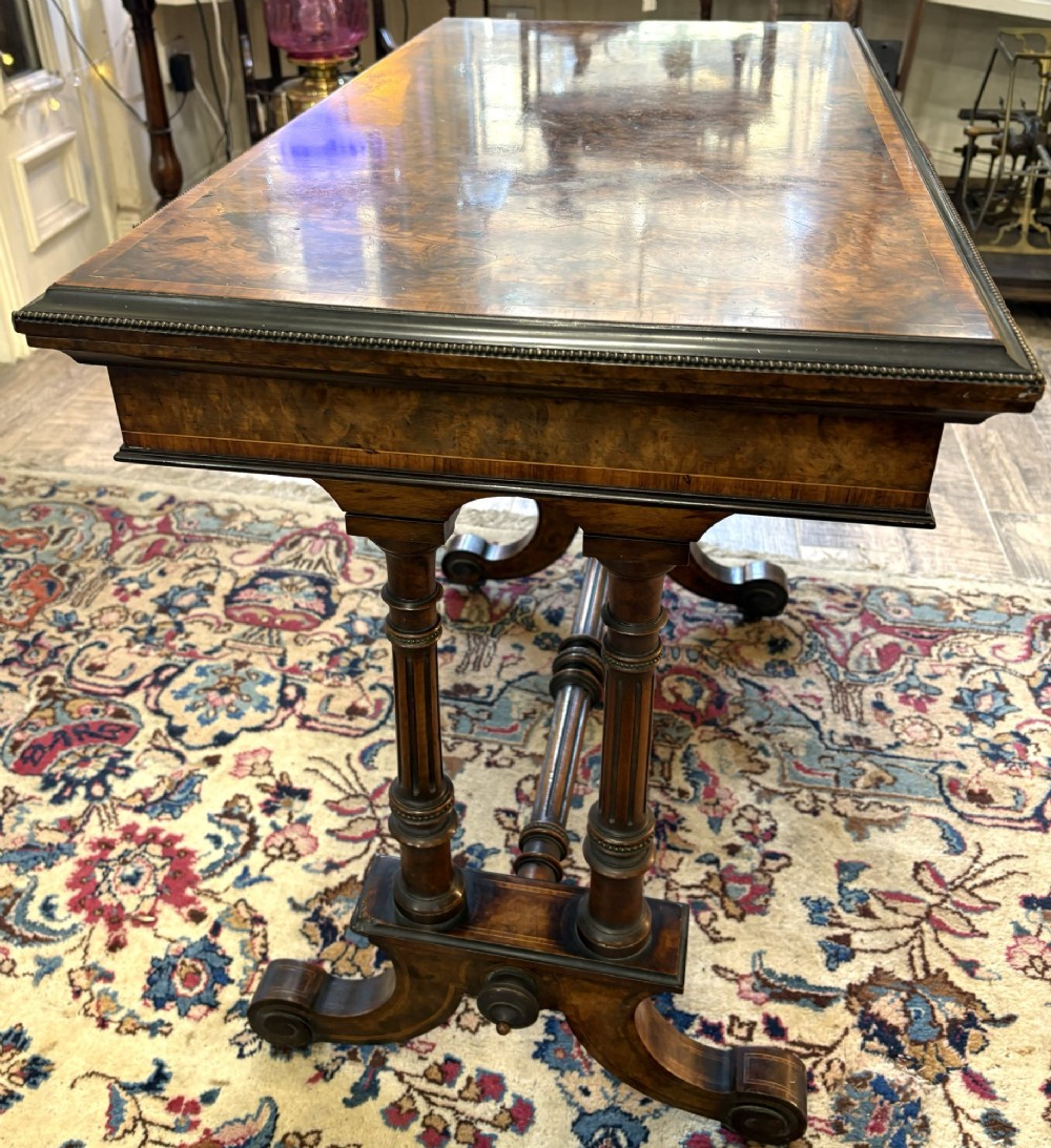 A Victorian burr walnut card table featuring ebonised bead moulding, crossbanded veneer top, twin turned pillar supports, and a turned stretcher base. View IV