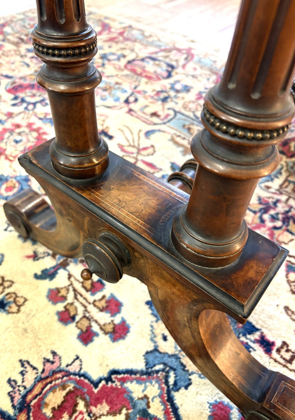 A Victorian burr walnut card table featuring ebonised bead moulding, crossbanded veneer top, twin turned pillar supports, and a turned stretcher base. View V