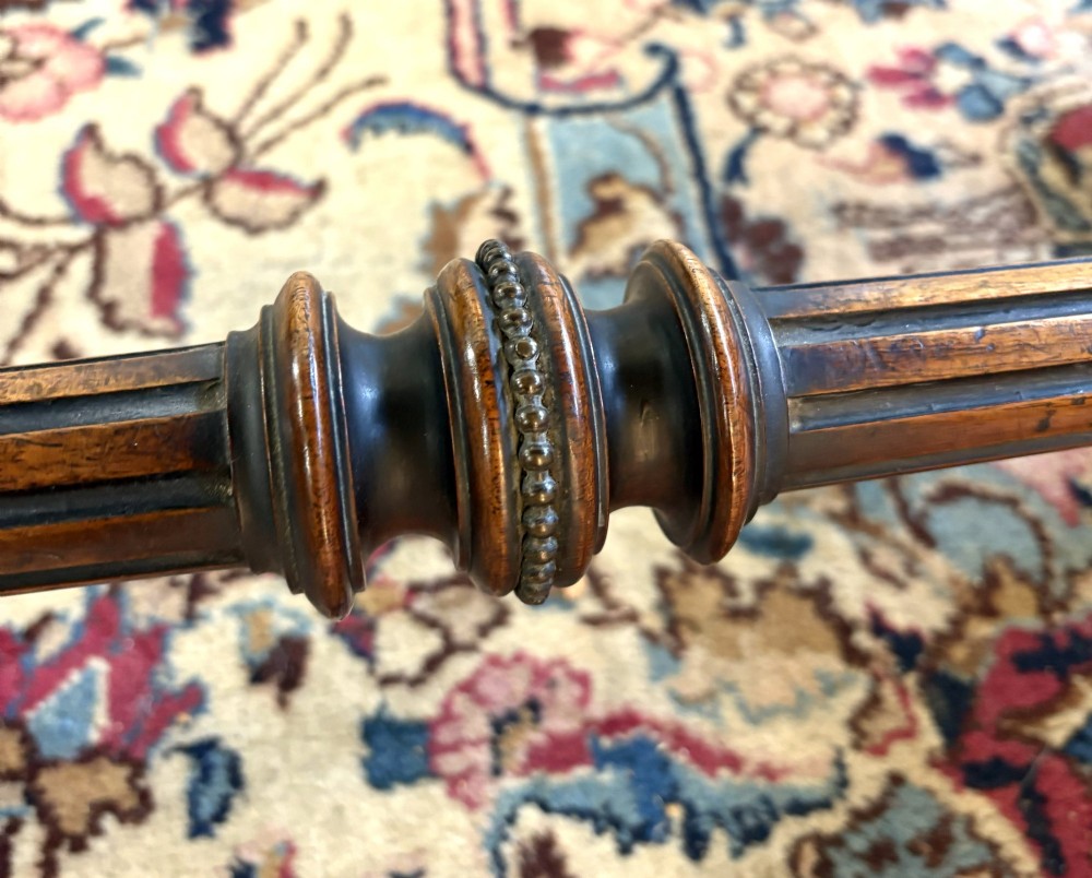 A Victorian burr walnut card table featuring ebonised bead moulding, crossbanded veneer top, twin turned pillar supports, and a turned stretcher base. View VI