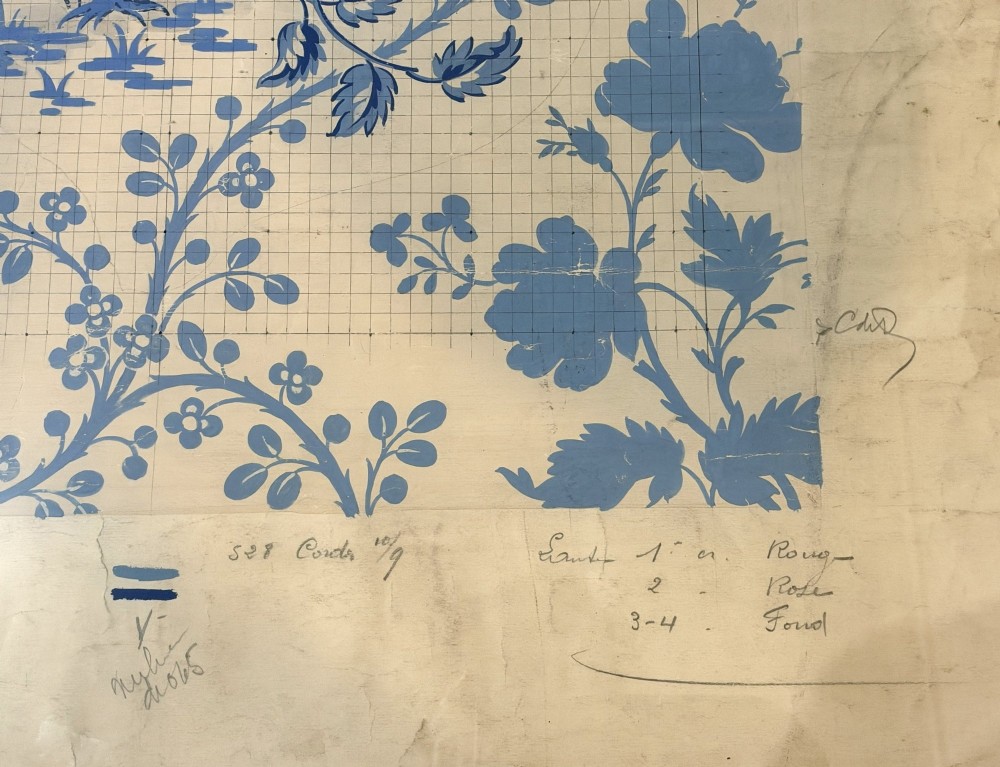 A framed vintage French textile design featuring a blue floral motif rendered on grid paper, complete with technical handwritten annotations and an original manufacturer label. View V