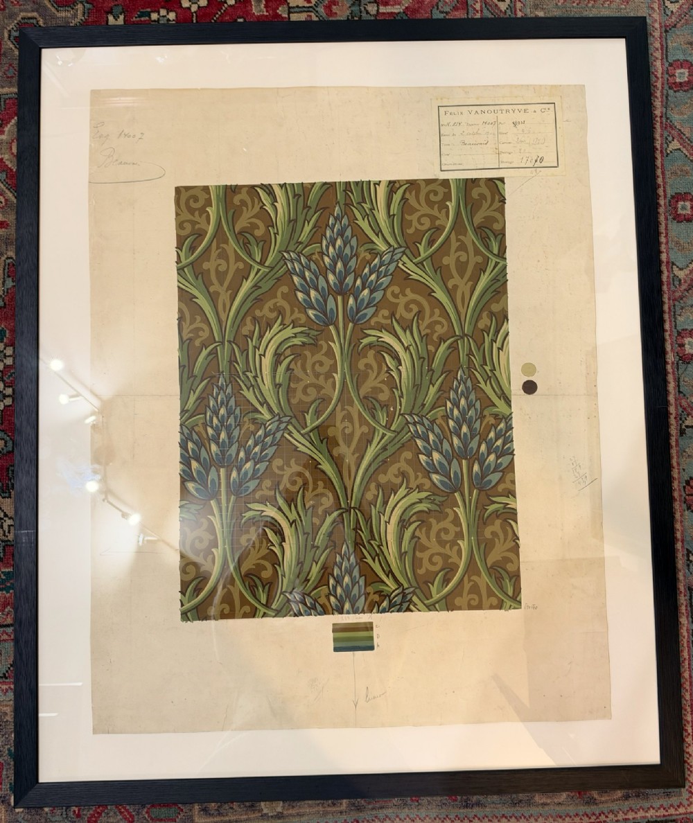 A framed antique French textile design on paper featuring stylized green leaves and blue botanical buds against a patterned brown background.