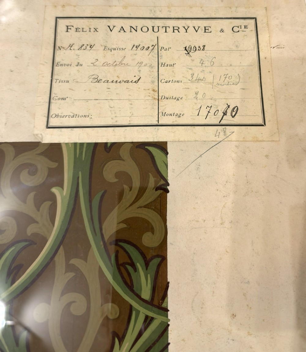 A framed antique French textile design on paper featuring stylized green leaves and blue botanical buds against a patterned brown background. View III