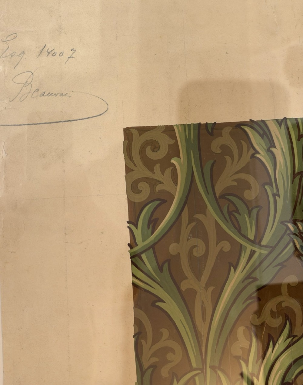A framed antique French textile design on paper featuring stylized green leaves and blue botanical buds against a patterned brown background. View IV