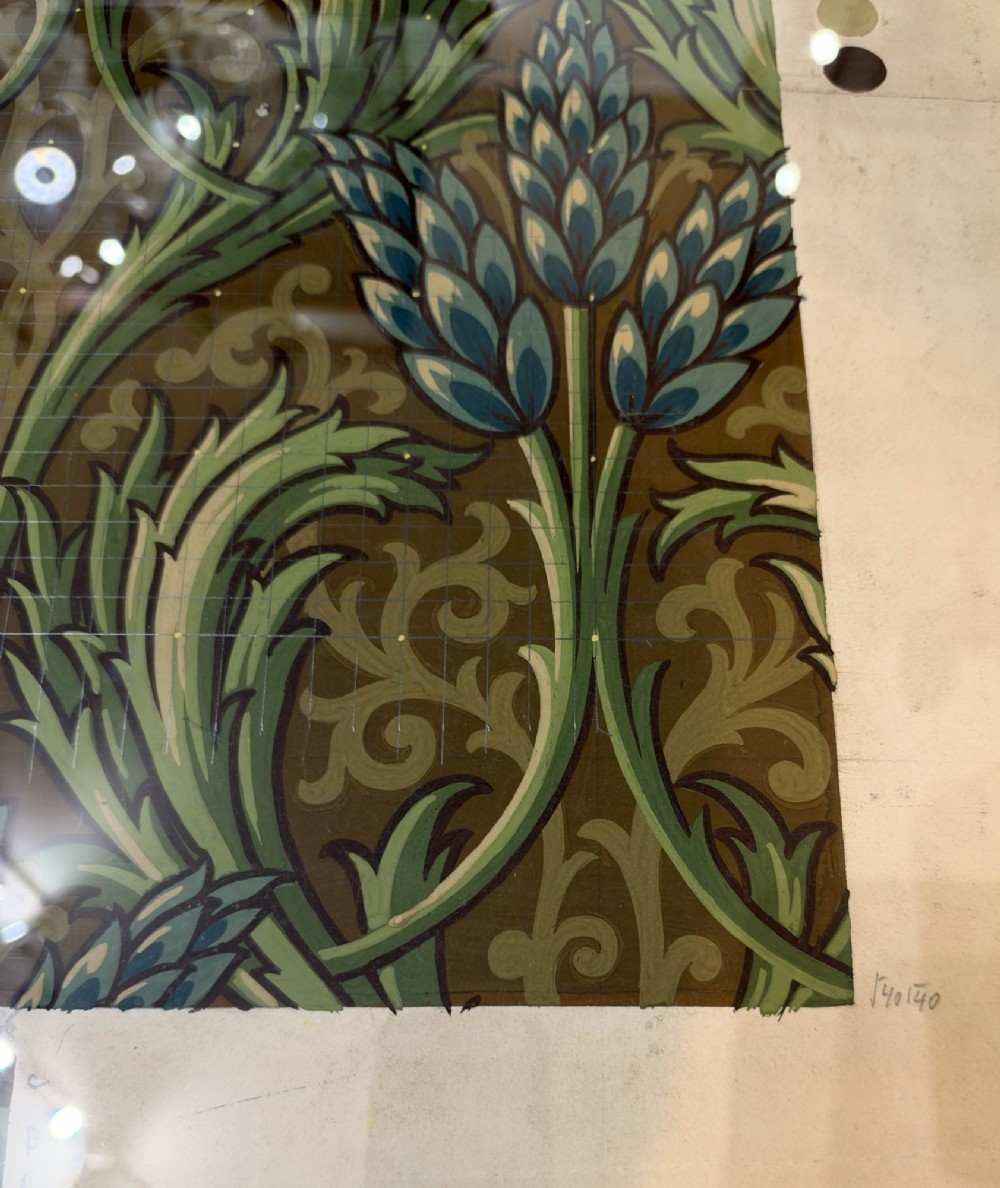 A framed antique French textile design on paper featuring stylized green leaves and blue botanical buds against a patterned brown background. View VI