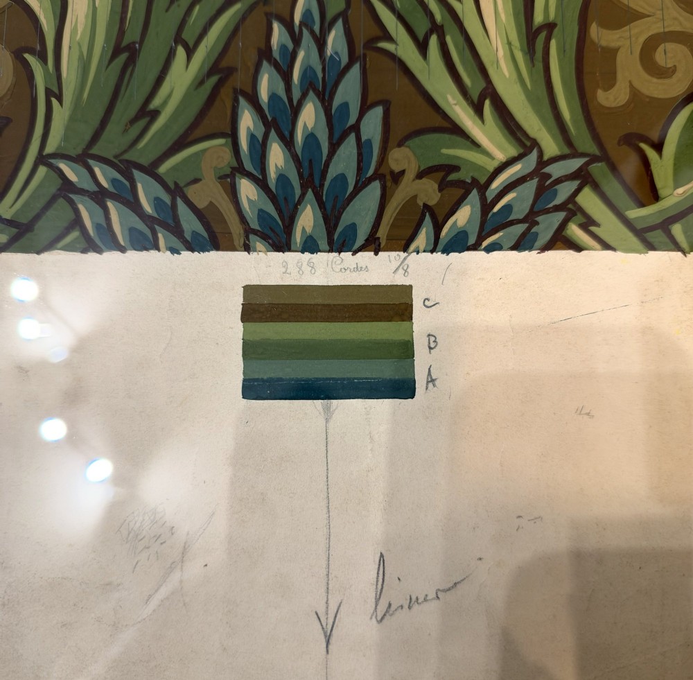 A framed antique French textile design on paper featuring stylized green leaves and blue botanical buds against a patterned brown background. View VII