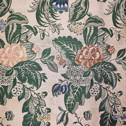 fig 1. An 18th-century floral woven Spitalfields silk panel with green leaves and pastel blossoms, presented inside a dark wood rectangular frame.