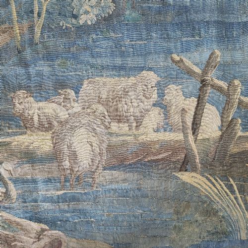 fig 2. An eighteenth-century Aubusson hand-woven tapestry depicting a pastoral landscape with a river, stone tower, thatched structure, and figures in shades of blue, green, and beige.