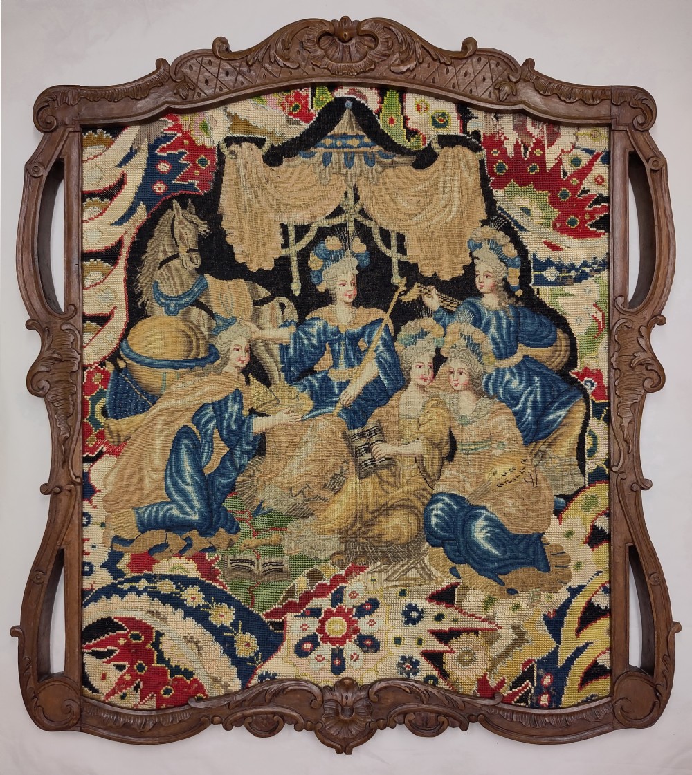 An antique framed needlework picture featuring figurative scenes in blue and cream stitches set within a carved wood Rococo frame.