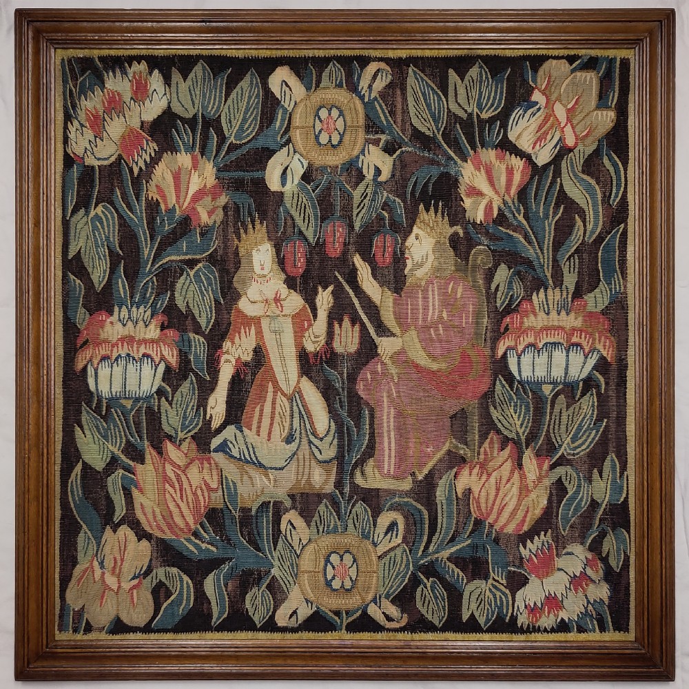 A framed 17th-century tapestry panel depicting two crowned figures surrounded by dense floral foliage in shades of pink, green, and brown.