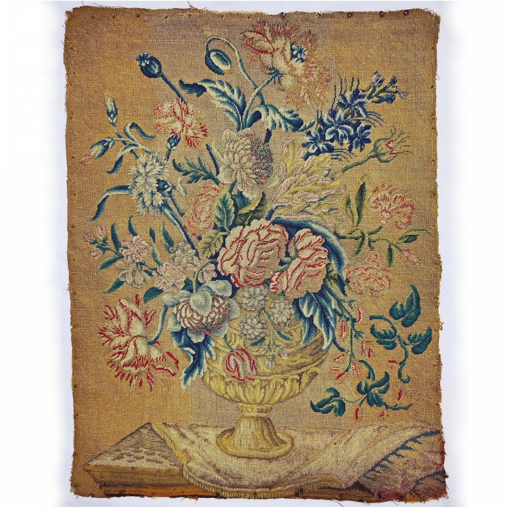 An 18th-century unframed needlework picture displaying a bouquet of colourful flowers in a golden urn on an ochre canvas background.