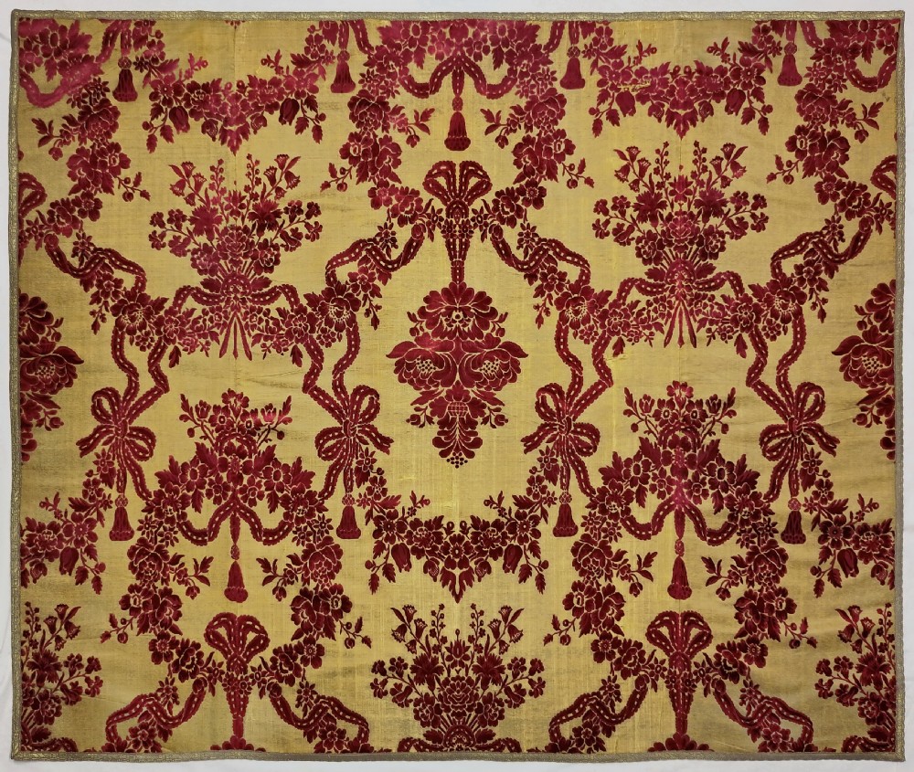 An 18th-century rectangular silk velvet wall hanging featuring crimson floral and bow motifs in cisele relief on a gold ground.
