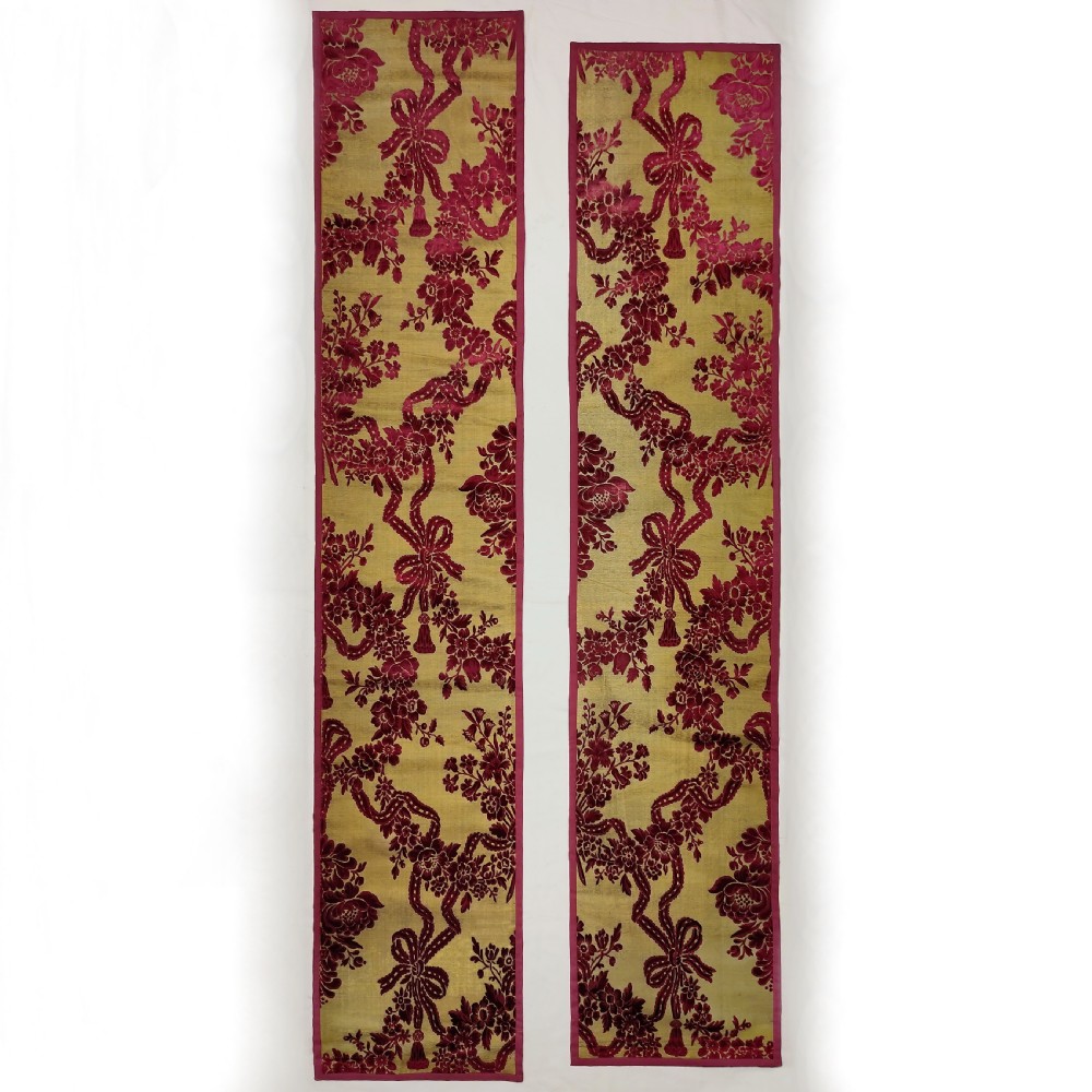 A pair of long vertical eighteenth-century cisele silk velvet panels featuring crimson floral and ribbon patterns on a gold ground.