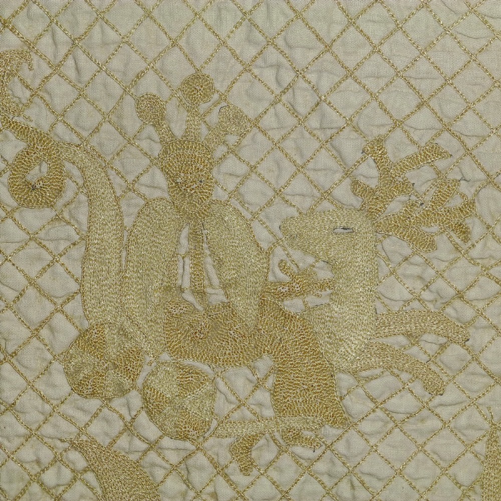 Close up view of a cream linen coverlet featuring diamond lattice quilting and detailed raised embroidery of a stag and heraldic figures.