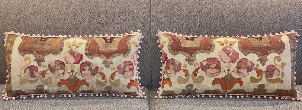 A pair of rectangular cushions made from 19th-century Aubusson tapestry with floral patterns in pink, terracotta, and cream, detailed with a pom-pom fringe.