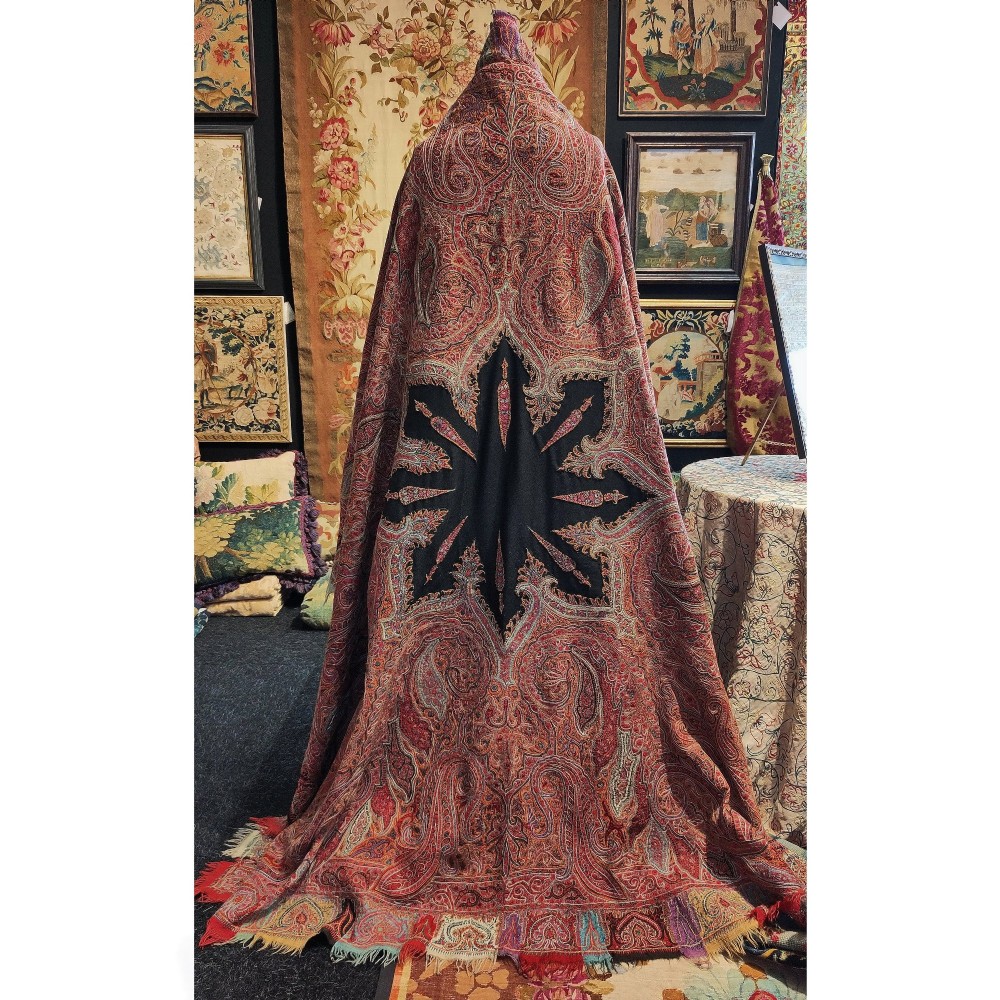 A square nineteenth-century embroidered Kashmiri shawl featuring dense red paisley boteh patterns surrounding a black star-shaped central medallion.