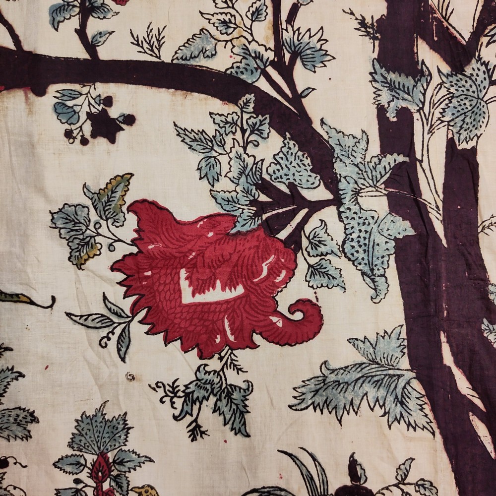 A rectangular 19th-century white cotton textile featuring a woodblock-printed tree of life design in red, green, and dark brown within an ornate floral border. View V
