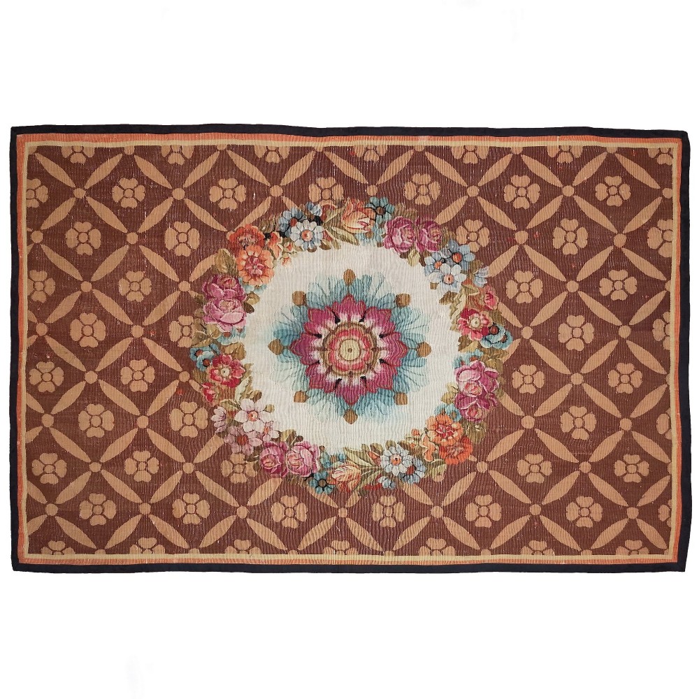 A rectangular 19th-century flatweave tapestry rug featuring a central floral medallion within a brown geometric lattice pattern.